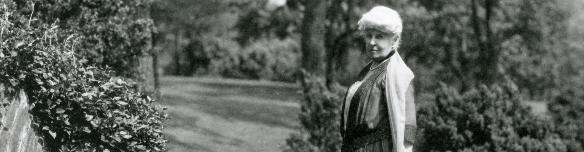 A black-and-white photograph of an woman standing in a garden.