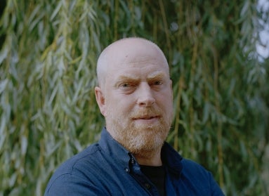 A headshot of a man standing outside wearing a blue button-down.