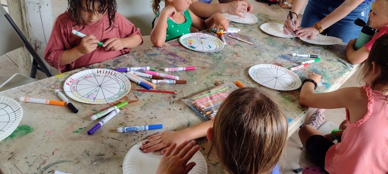 A group of young summer campers draw with markers on paper plates.