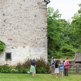 A group of people dressed in business casual look at a plant growing along a stone building.