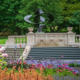 A sculpture atop a step fountain surrounded by flowers. 