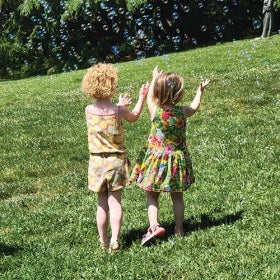 Two young girls in dresses run through a field of bubbles.
