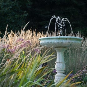 A decorative water fountain surrounded by brown, purple, and green foliage.
