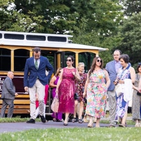 A group of people in bright, flowery attire step off a trolley. 