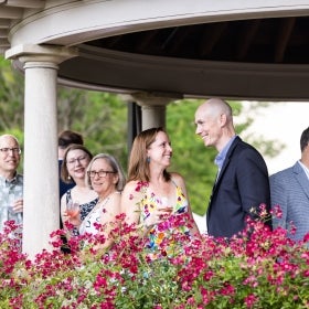 A group of people mingling under a gazebo surrounded by blooming roses.