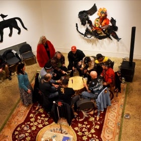 The Lenape Nation of PA sitting in a circle around a large drum and performing. 