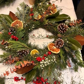 A holiday wreath decorated with pine cones, bright red holly berries, dried rounds of citrus, and other foliage. 