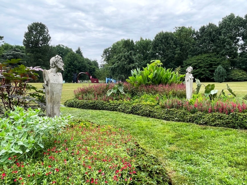 A garden in bloom with paisley-shaped beds and two statues at a distance facing each other on a gray day. 