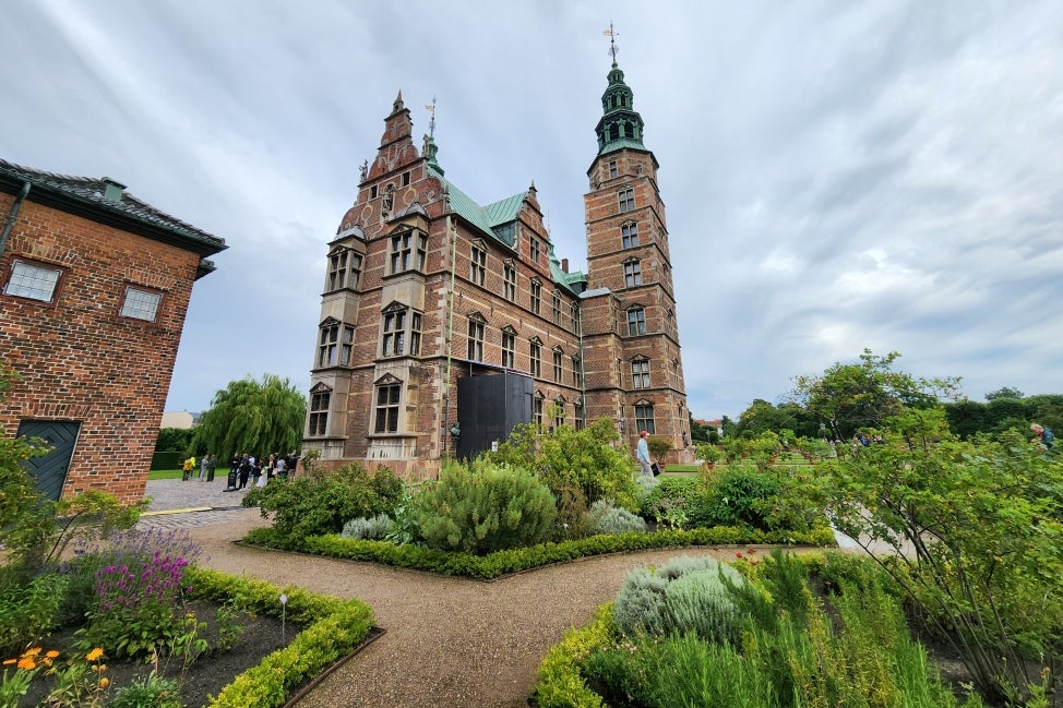 The Rosenborg Castle surrounded by garden beds in bloom on a cloudy day. 