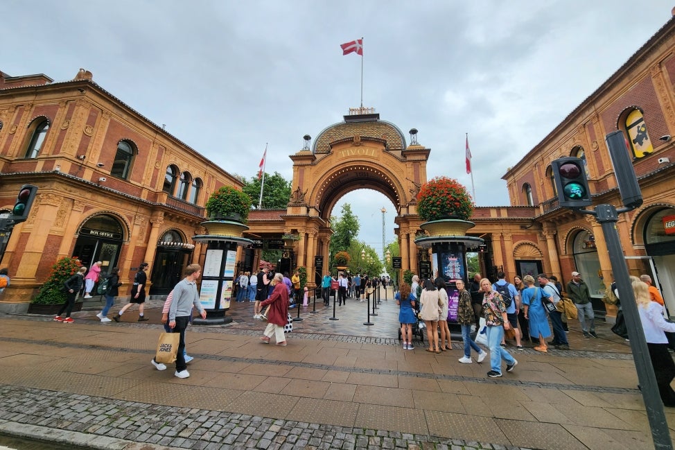 A main entrance to a botanical garden with a large terracotta-colored building with an entrance arch and people walking around on a cloudy day. 