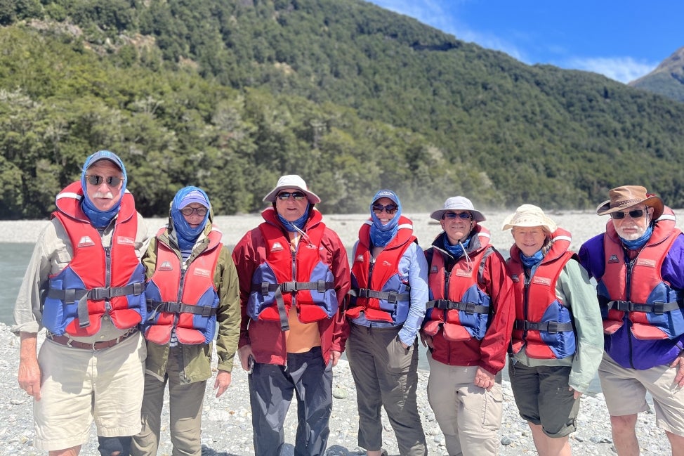 A group of people wearing red life vests stand outside in front of mountains.