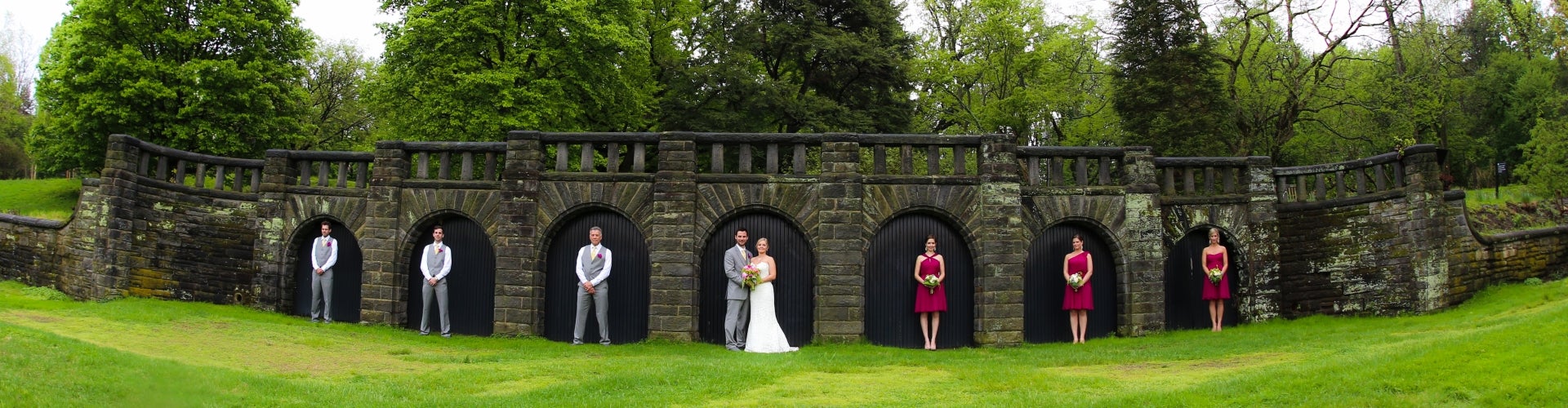 A wedding party stands in front a stone wall, each in their own archway.