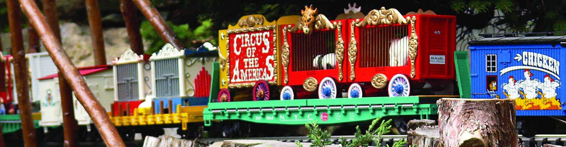 A circus-themed model train riding on a wooden track. 