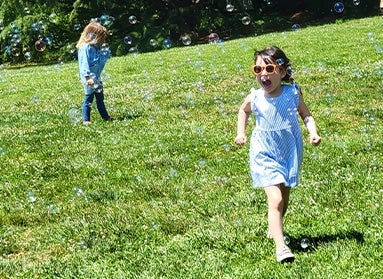 Two young girls in a green field filled with bubbles. 