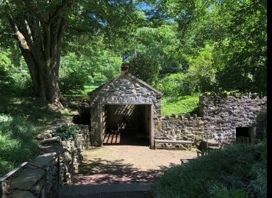 A stone springhouse surrounded by trees and green foliage.