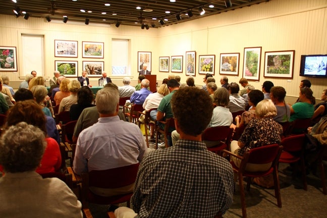 A large group of people sit in chairs facing a speaker. 