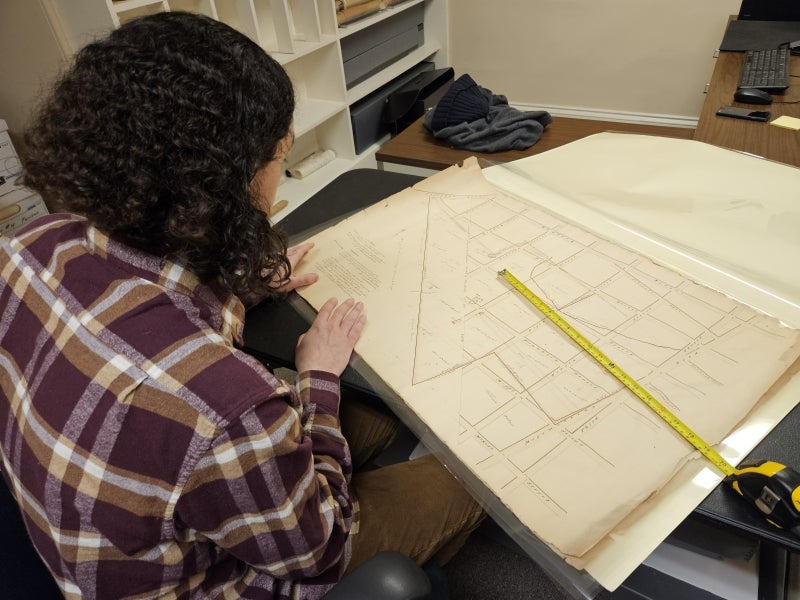 A person sits in front of an old map with yellow measuring tape. 