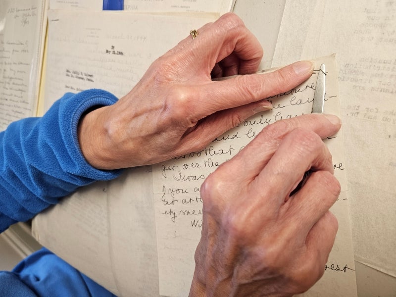 The hands of an archivist removing carefully removing a rusty staple from a piece of paper with handwriting on it.